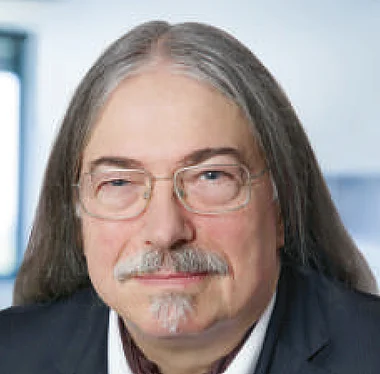 Ein Mann in Anzug und Hemd, lächelnd, professionelles Porträt.