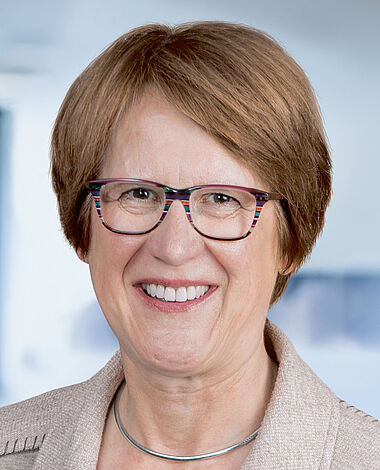 Lachende Frau in Brille und Blazer, professionelles Porträt.