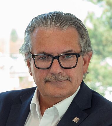 Ein Mann im Anzug lächelt freundlich in die Kamera.