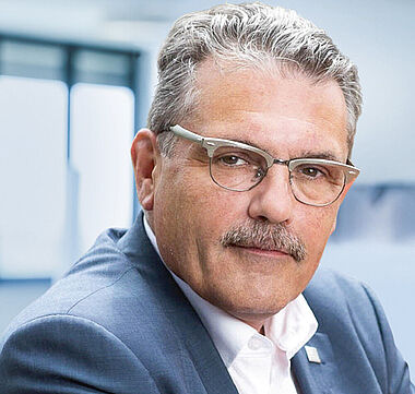 Ein Mann im Anzug lächelt freundlich in die Kamera.