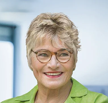 Professionelle Porträt einer lächelnden Frau in einem grünen Blazer.