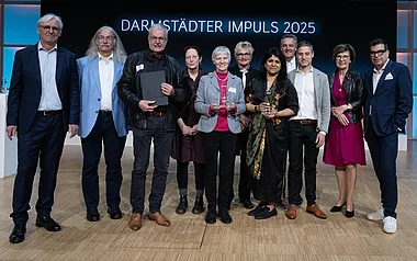 Personen in Anzügen und Kleidern posieren mit einem Preis auf einer Konferenz.